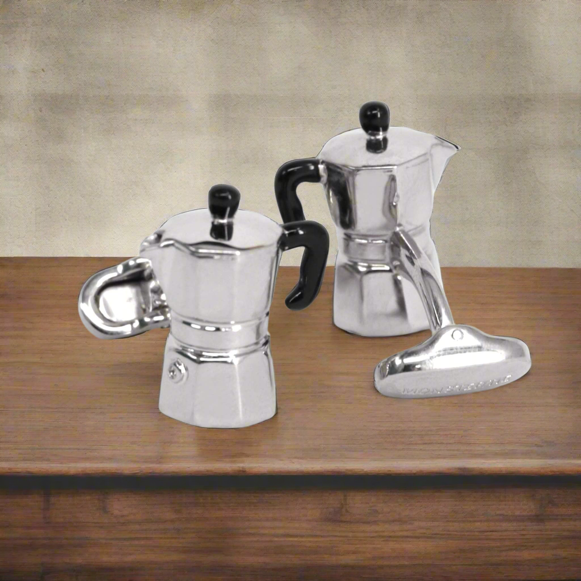 Two silver espresso pots with black handles on a wooden surface.