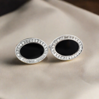A pair of oval-shaped black enamel cufflinks with crystal embellishments around the edge, displayed on a white background.