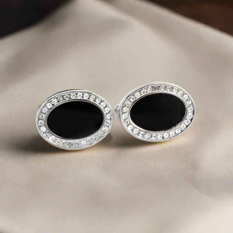 A pair of oval-shaped black enamel cufflinks with crystal embellishments around the edge, displayed on a white background.