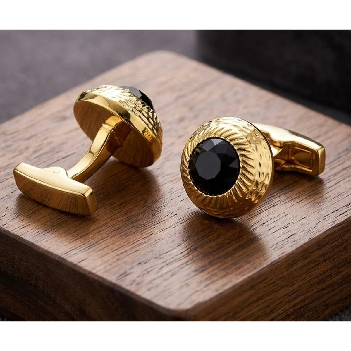 A pair of men's gold cufflinks with textured circular faces and central black oval stones, displayed on a dark wood block.