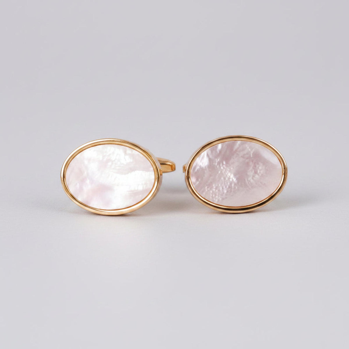 A pair of oval gold cufflinks with white mother of pearl accents on a white background.