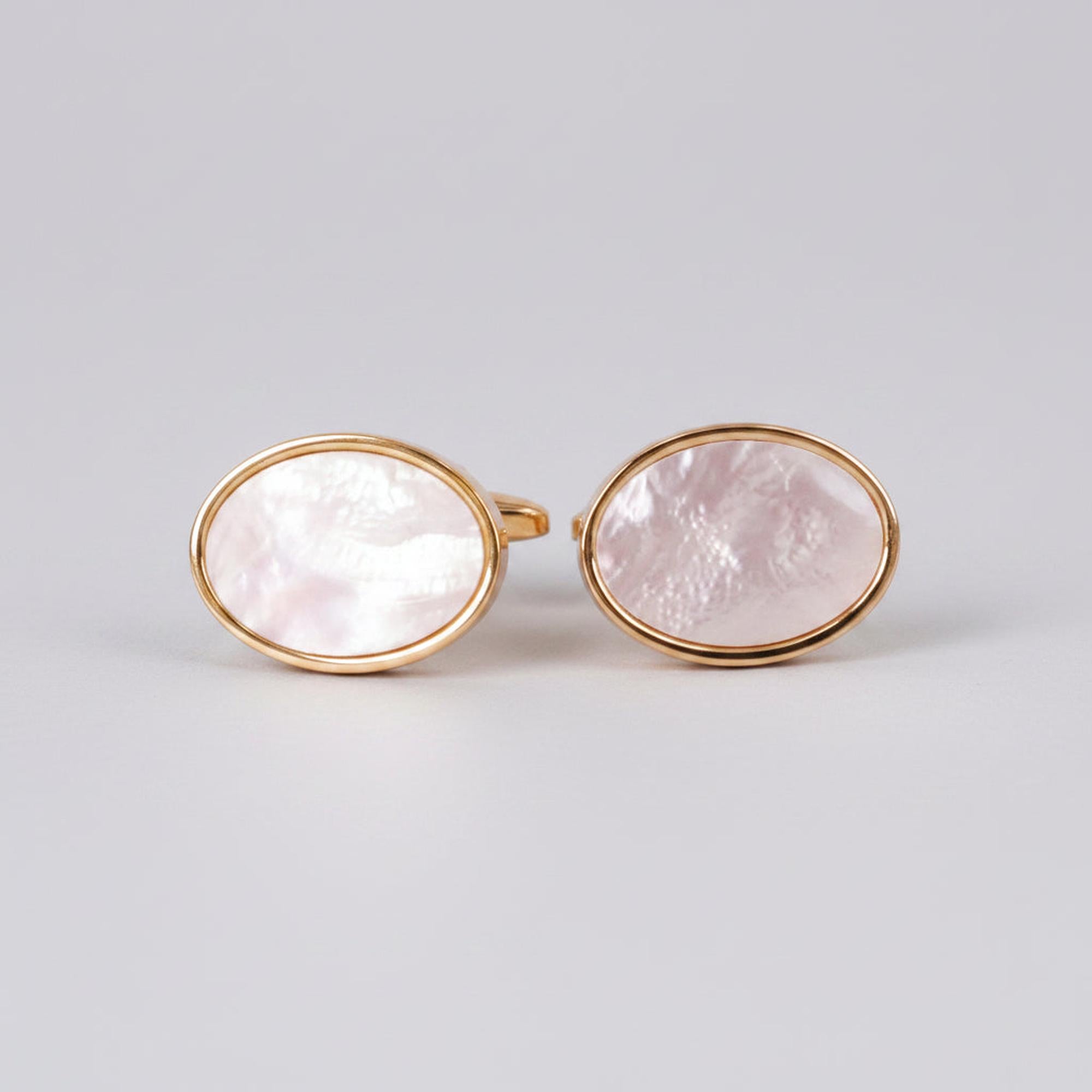 A pair of oval gold cufflinks with white mother of pearl accents on a white background.
