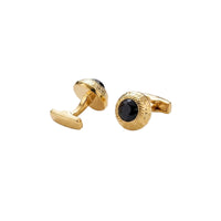 A pair of gold cufflinks with textured circular faces and central black oval inlays, photographed on a clean white background.