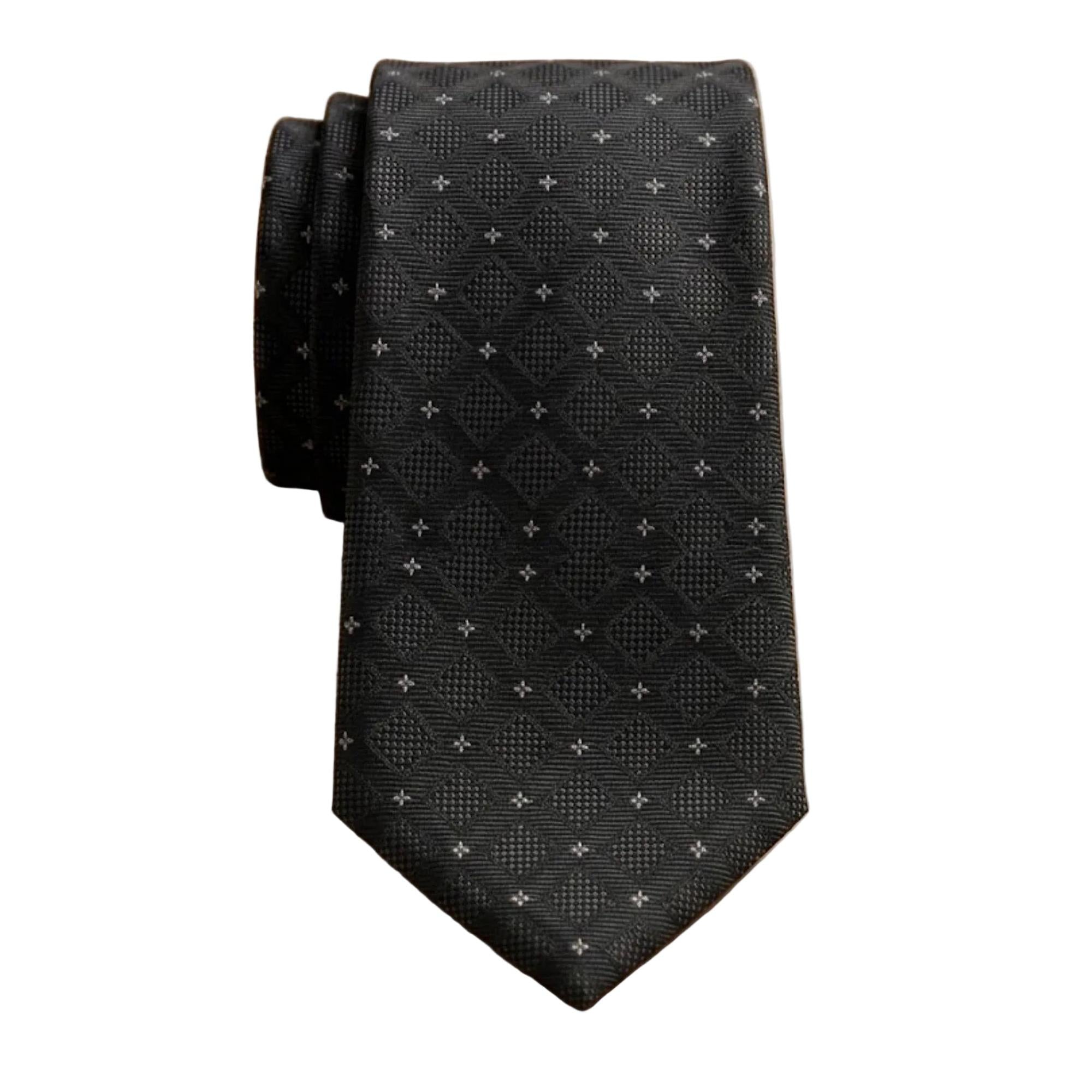 A black textured necktie with a small white geometric pattern, folded on a light wood grain surface.