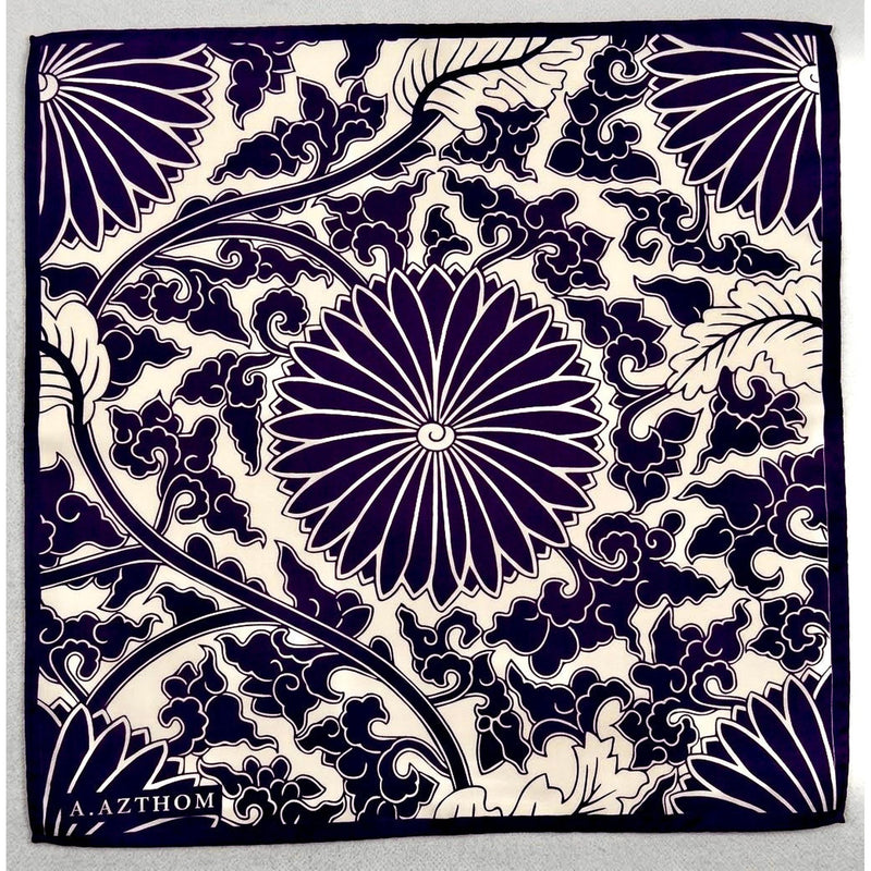 A square pocket squre  featuring a navy blue and cream floral pattern with a central chrysanthemum and swirling vine motifs. The brand name 'Azthom'