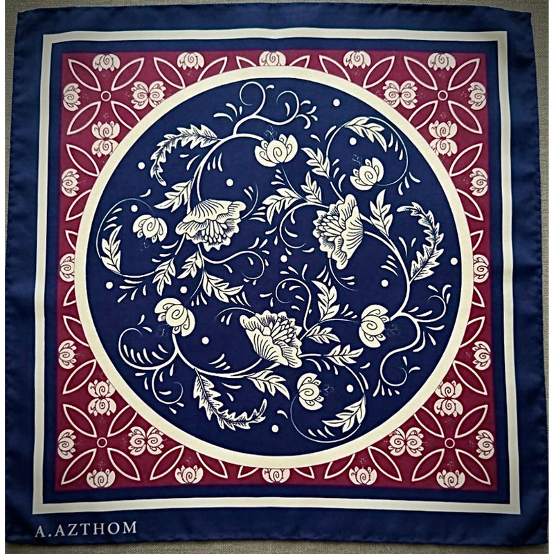 A square silk scarf featuring a classic botanical pattern with a navy blue center, a red border, and cream accents. The brand name 'A.