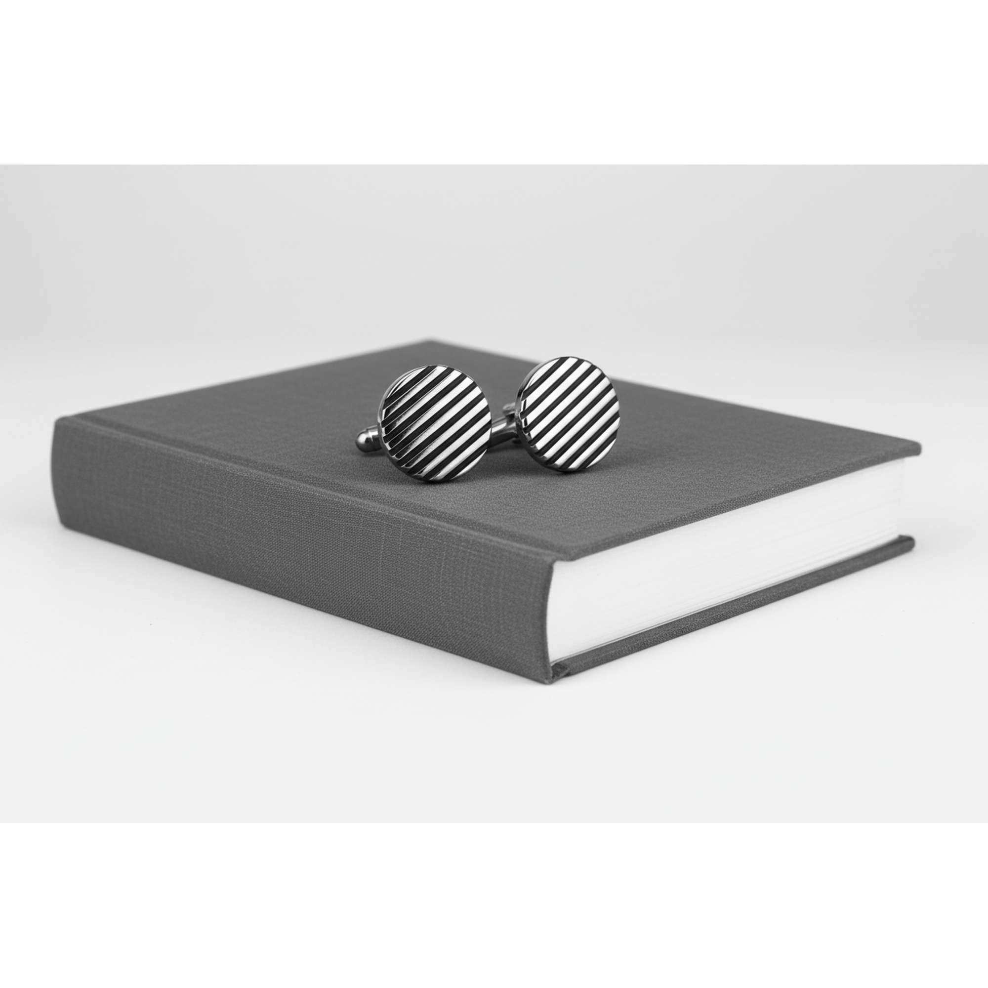 Black horizontal stripe cufflinks on a grey book, showcasing a modern design for formal attire.