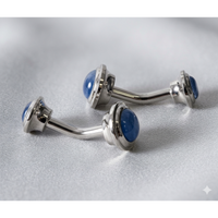 Two silver-toned curved barbell piercings with round blue cateye, displayed on a textured light gray fabric background.