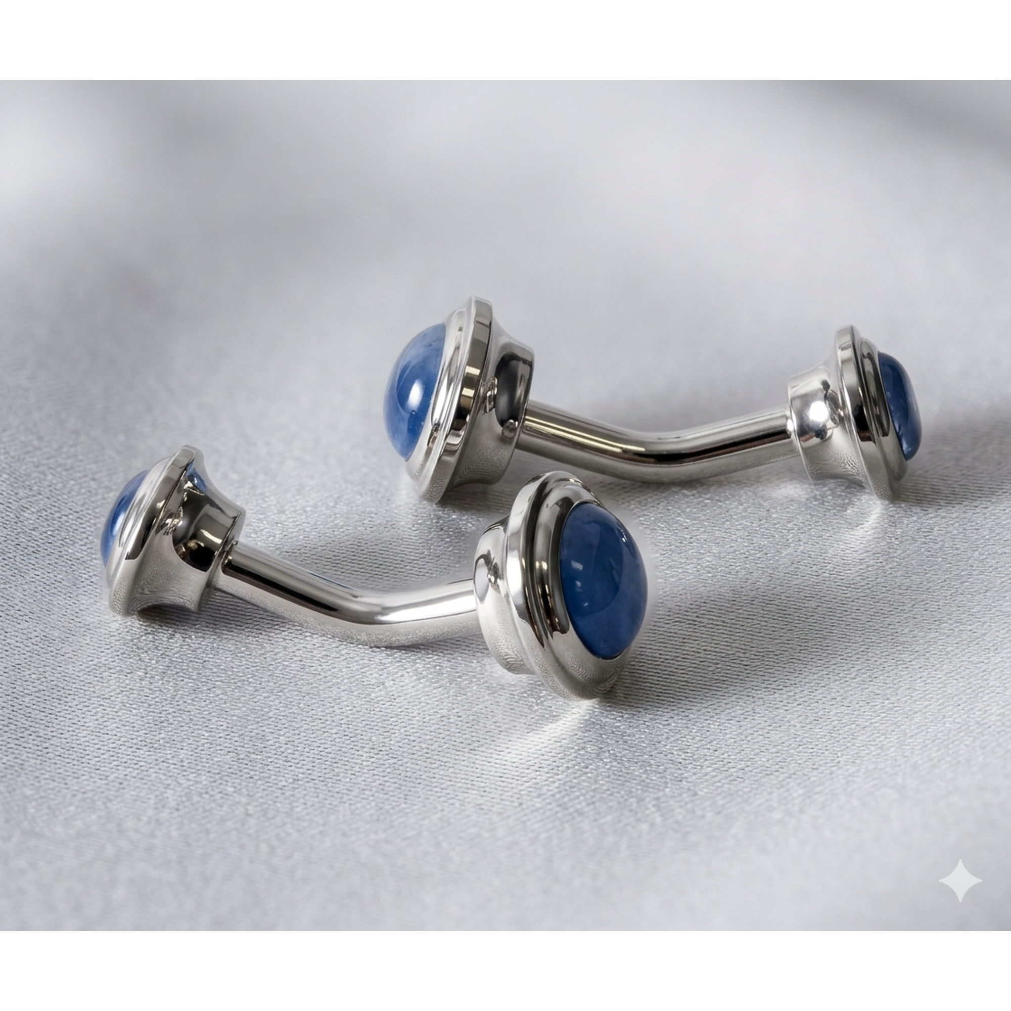 Two silver-toned curved barbell piercings with round blue cateye, displayed on a textured light gray fabric background.