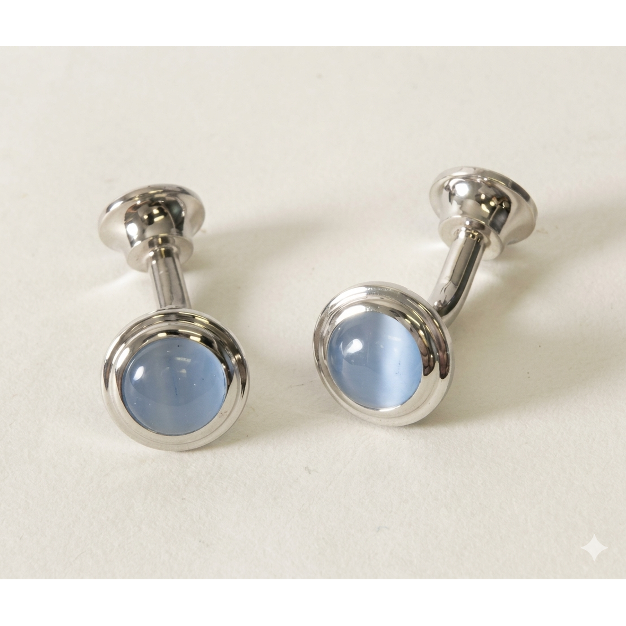 A pair of silver-toned cufflinks with oval light blue cateye, displayed on a clean off-white background.